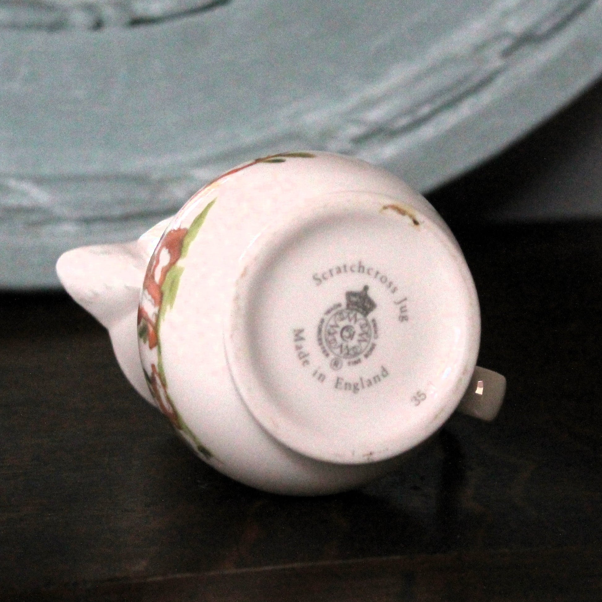 A vintage Royal Worcester porcelain jug shown upside down on a dark wooden surface, displaying its printed 'Scratchdown No. 36 Made in England' mark. 