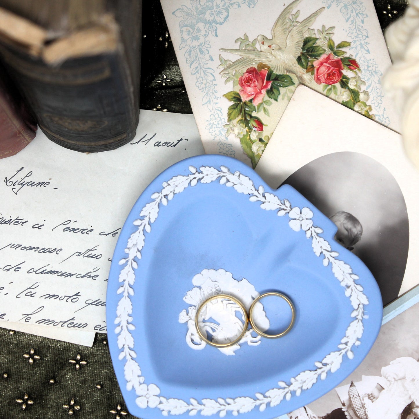 Blue heart-shaped Wedgwood jewelry dish with two gold rings on a vintage-style background