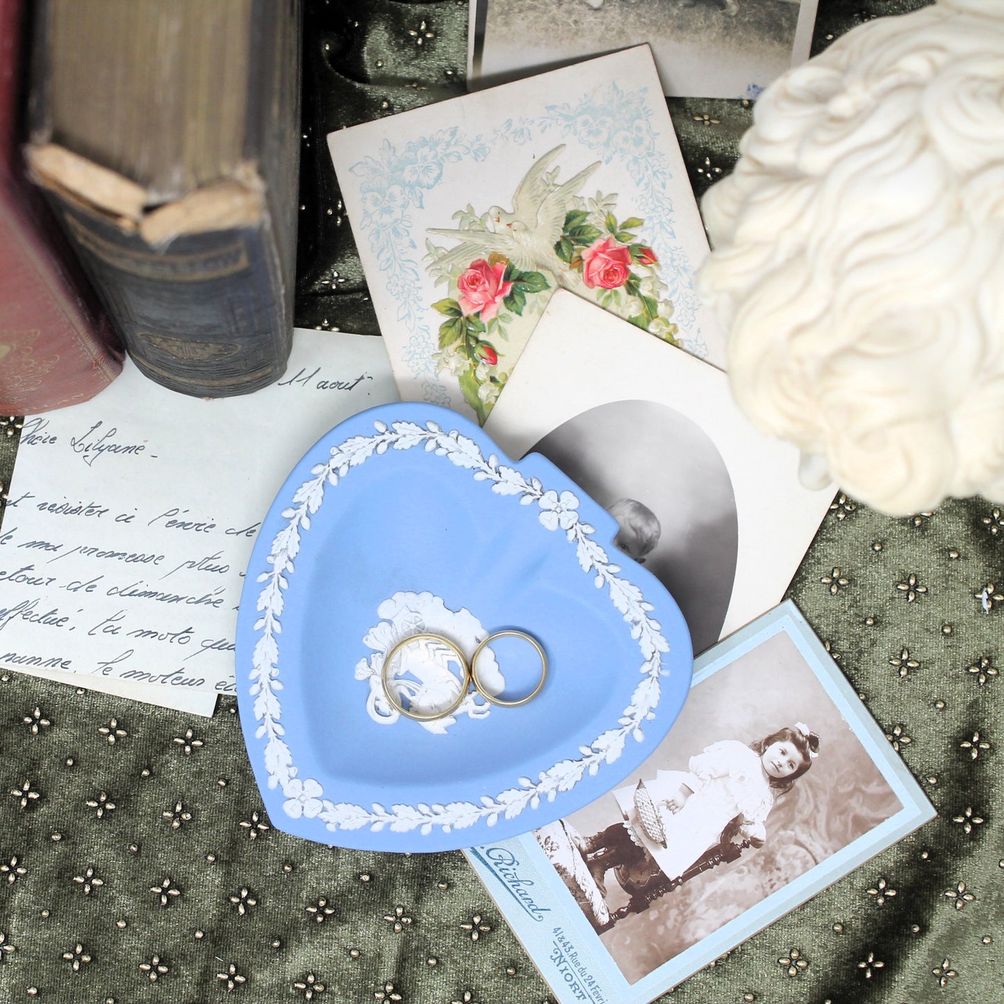 Heart-shaped blue jewelry dish with rings on a vintage-style background with photos and books.