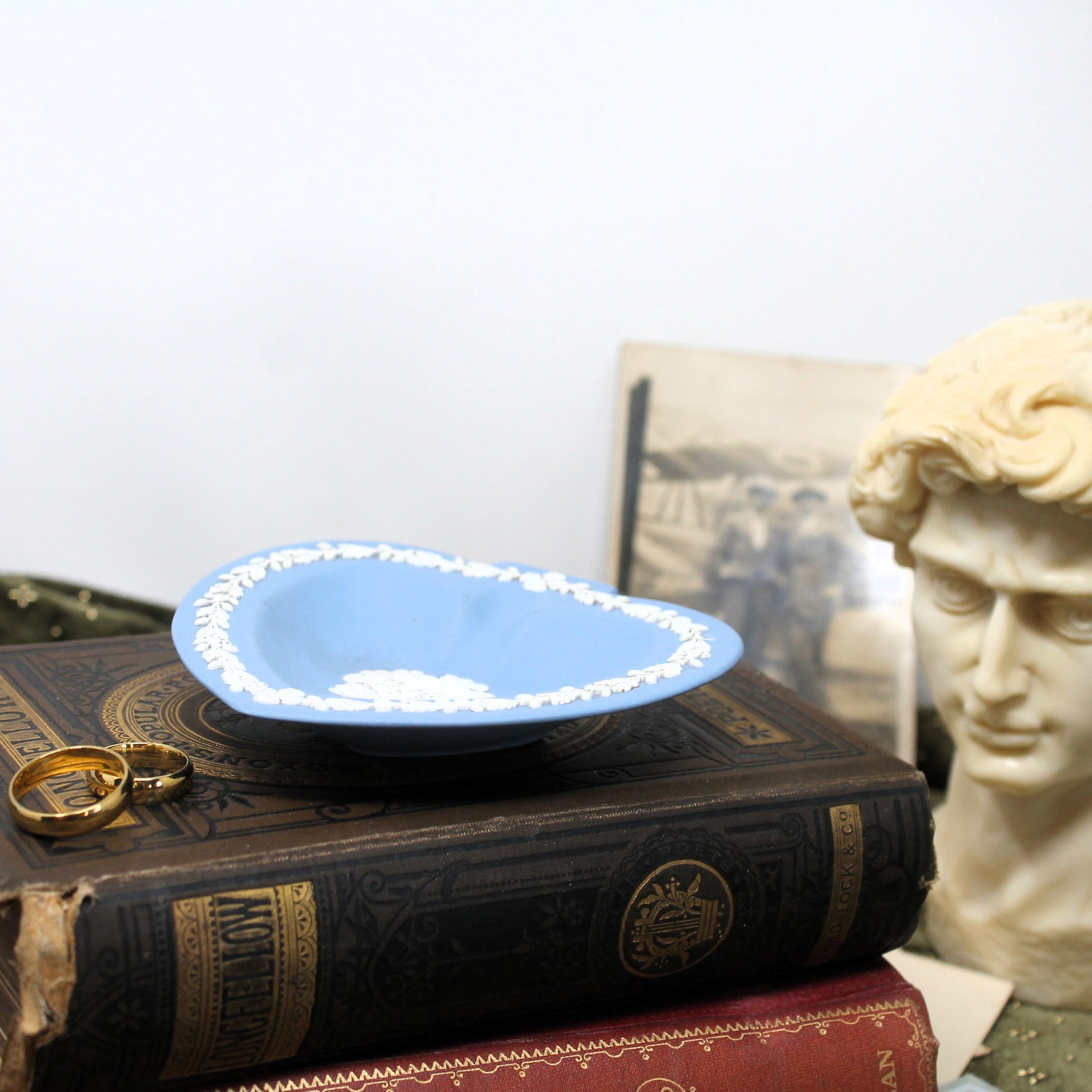 Blue dish with gold rings on a stack of books, classical statue in the background