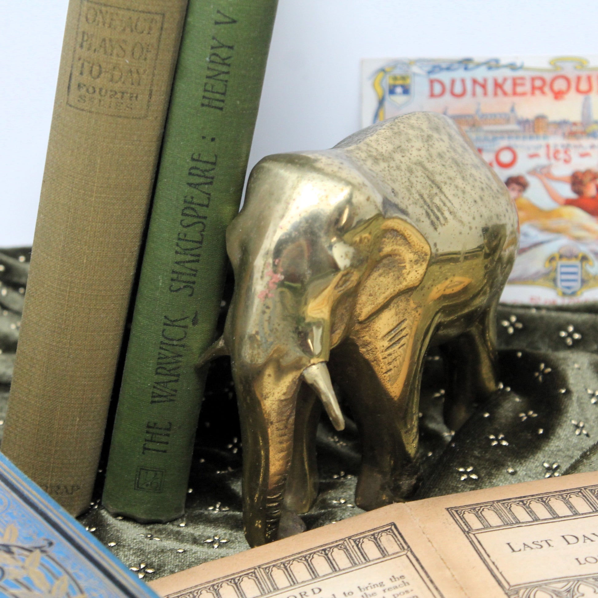Brass elephant figurine bookend holding up vintage books on a dark textured surface.