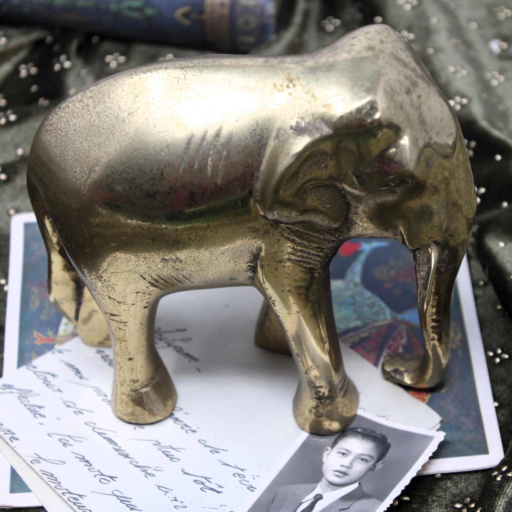 Quality arisan-made copper and brass cast elephant statue standing on top of scattered vintage papers and photographs.