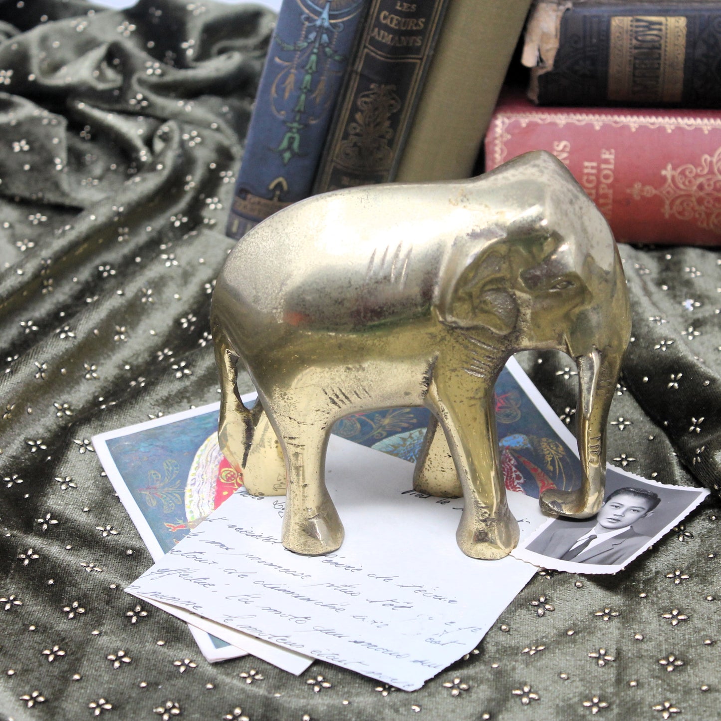 Vintage  elephant figurine cast in copper, brass finish, styled on top of vintage papers and books against a dark green patterned fabric backdrop.
