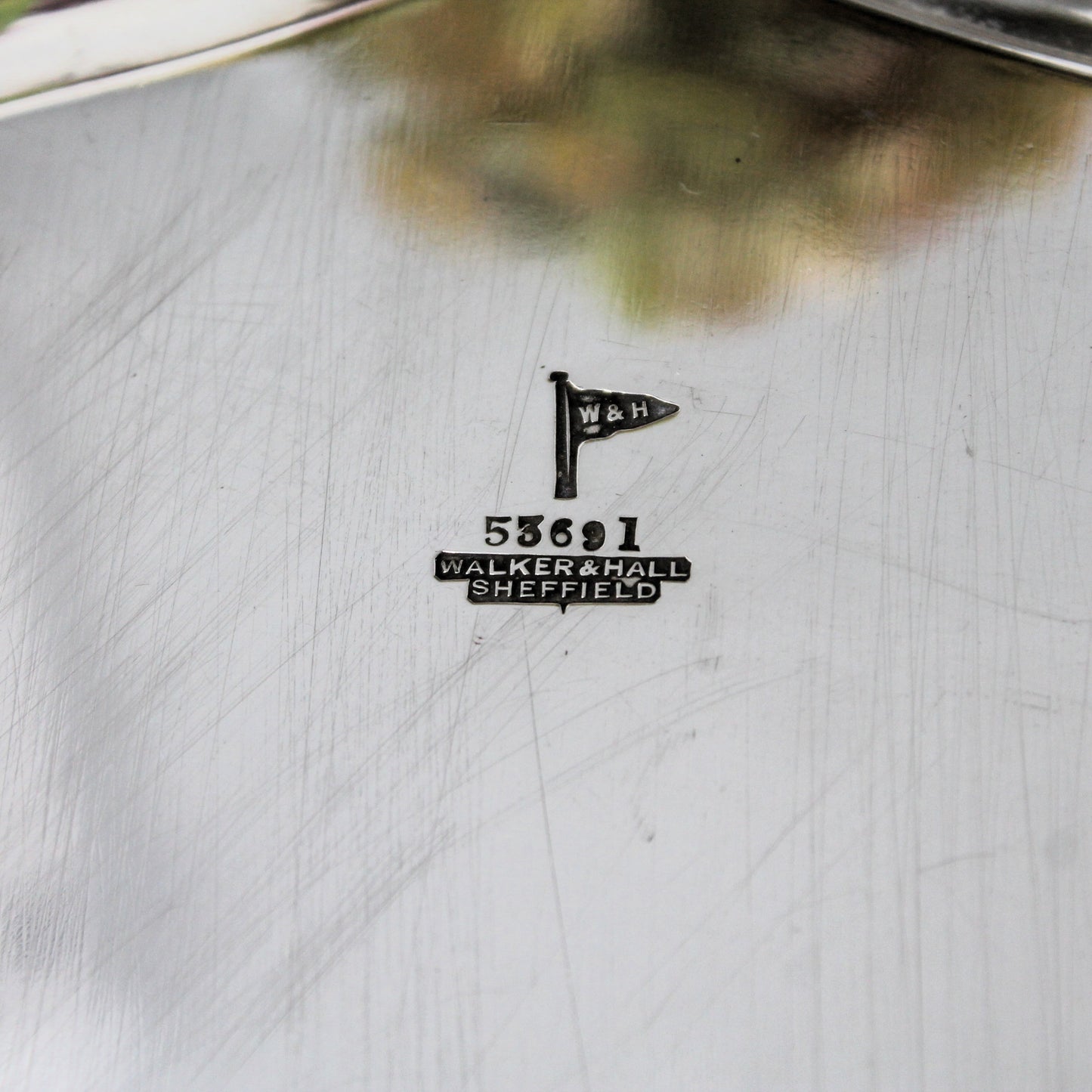Close-up of a sterling  silver tray with a small black engraved maker's mark reading W&H and Walker & Hall Sheffield, plus the number serial 53691.