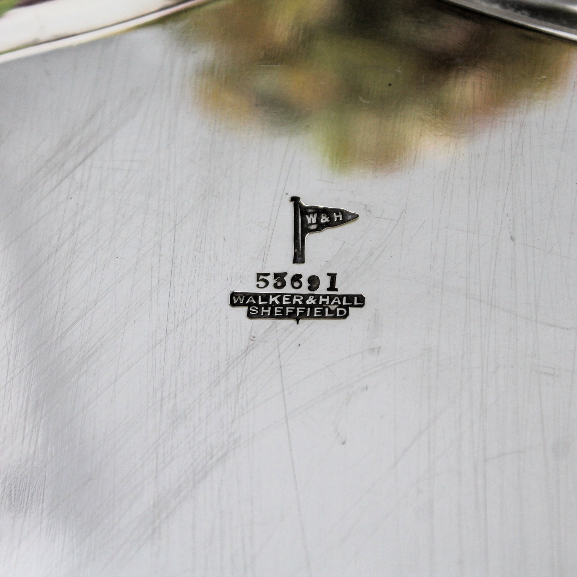 Close-up of a sterling  silver tray with a small black engraved maker's mark reading W&H and Walker & Hall Sheffield, plus the number serial 53691.