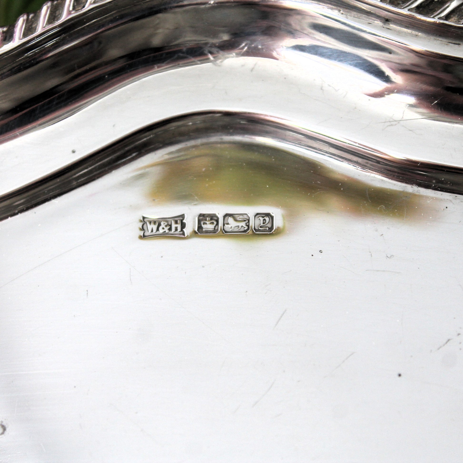 Close-up of the inside of a polished silver serving dish or tray, showing a small sterling silver hallmark with 'W&H' for Walker & Hall,  a crown for Sheffield silver, a lion to show it is Sterling silver, the Gothic letter Y for 1906