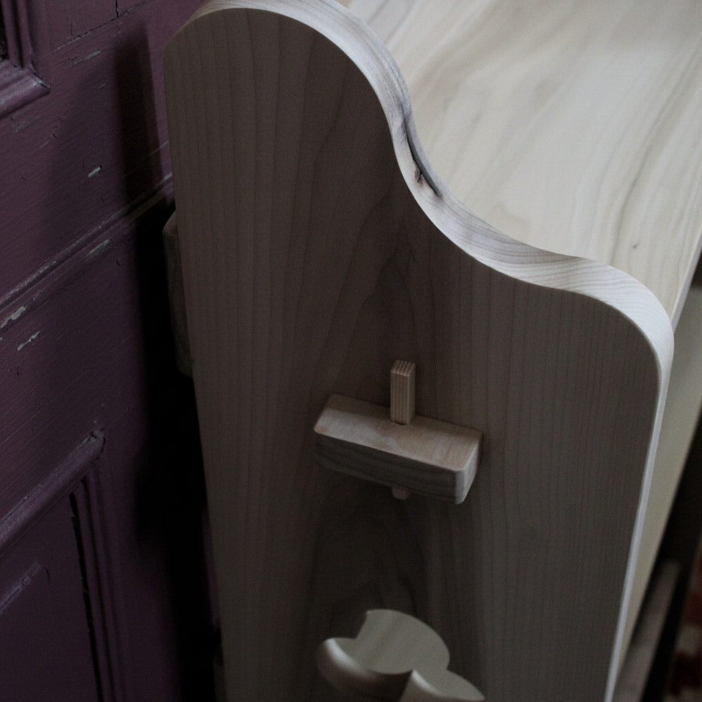 Close-up of a light gray wood cabinet or drawer front with a curved top edge and a small wooden pull or knob, shown against a beige wall.