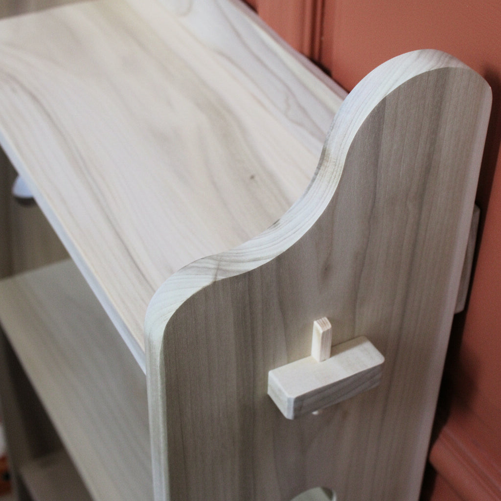 Close-up of a light gray wood-grain shelf or cabinet corner with a white peg or hook attached to the side panel.
