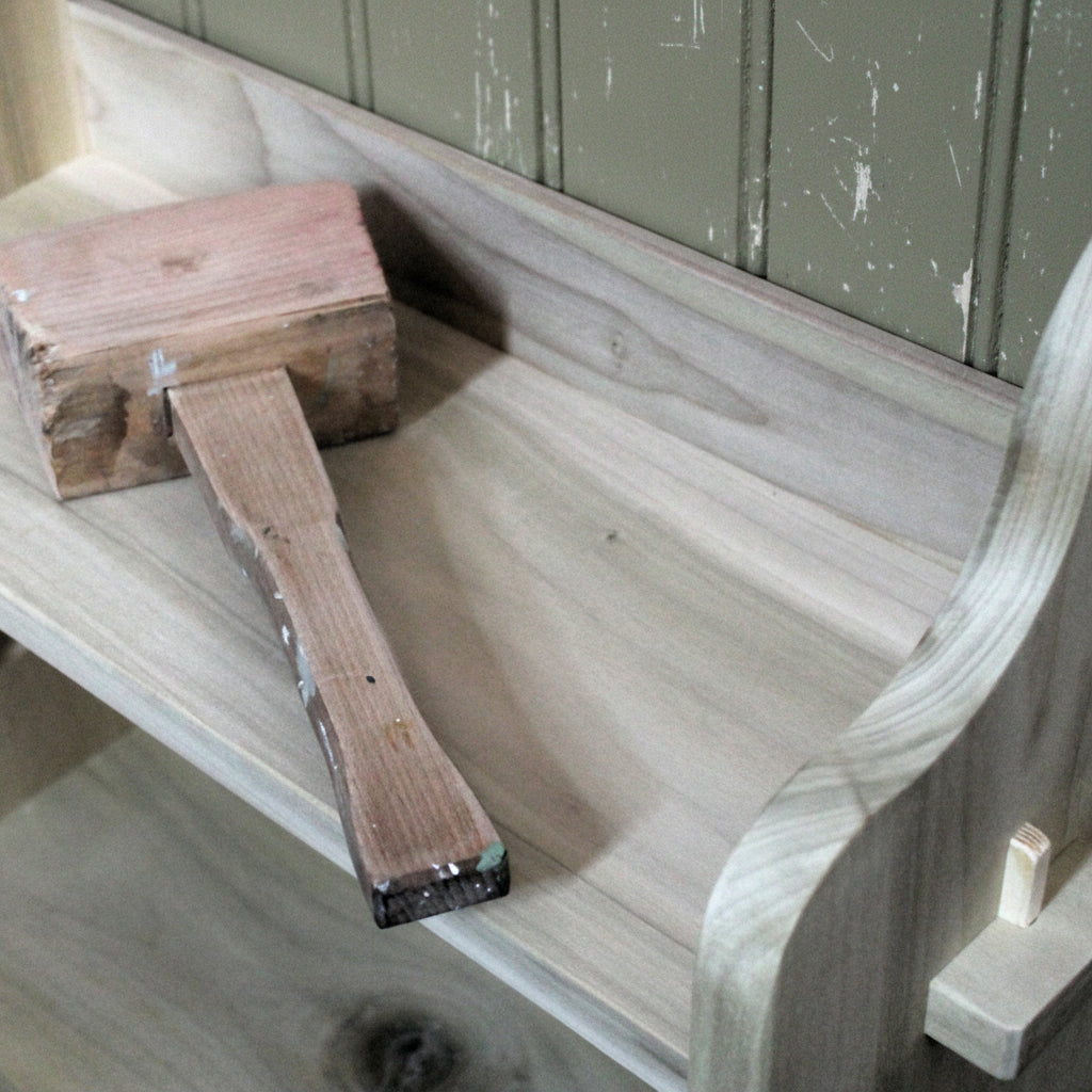 A wooden mallet tool with a worn pinkish-brown head and a light wood handle, resting on a bookcase after being used to knock in pegs in the seadley bookcase.  