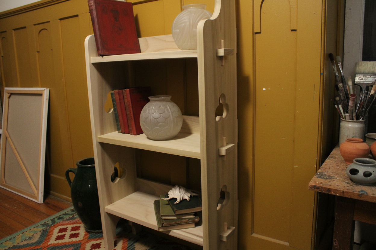 A light natural wood ladder shelf pegged sides, shown in a room setting with books and vases on its shelves
