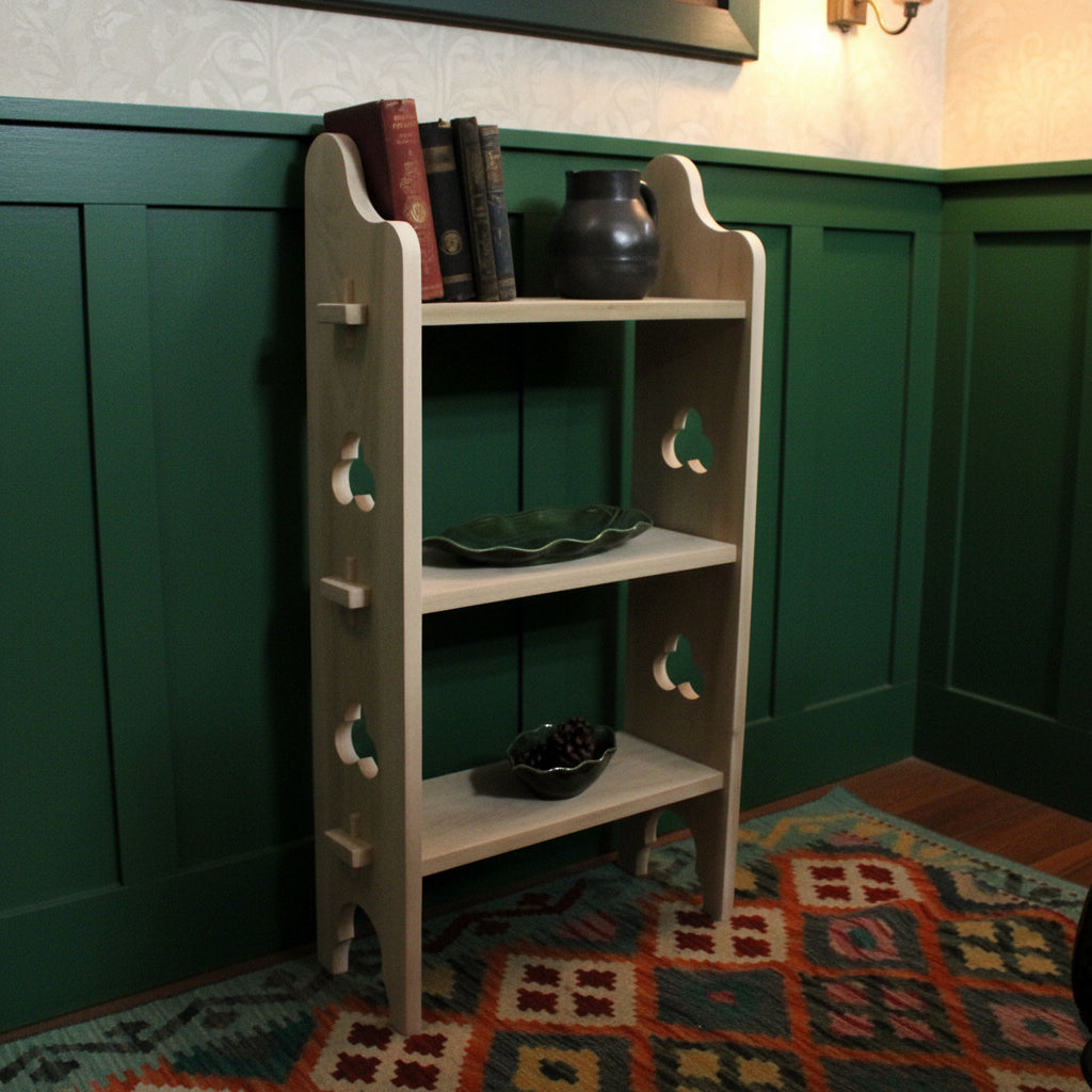 A light natural wood corner bookshelf with three shelves, decorative cutout details on the side, and small wooden pegs, shown holding books and decorative items in a room setting.