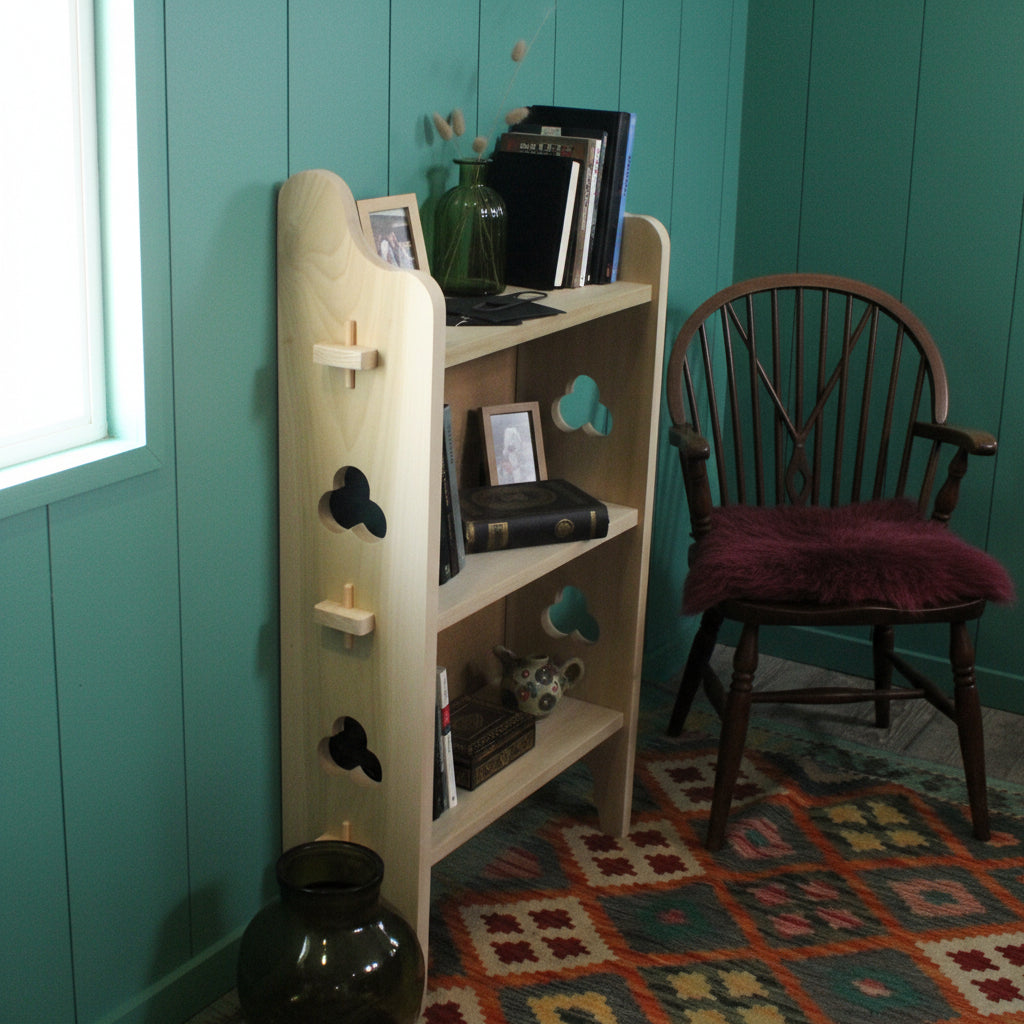 A light natural wood three-tier bookshelf with decorative cutout shapes on the side, styled with books and glass vases in an indoor room setting.