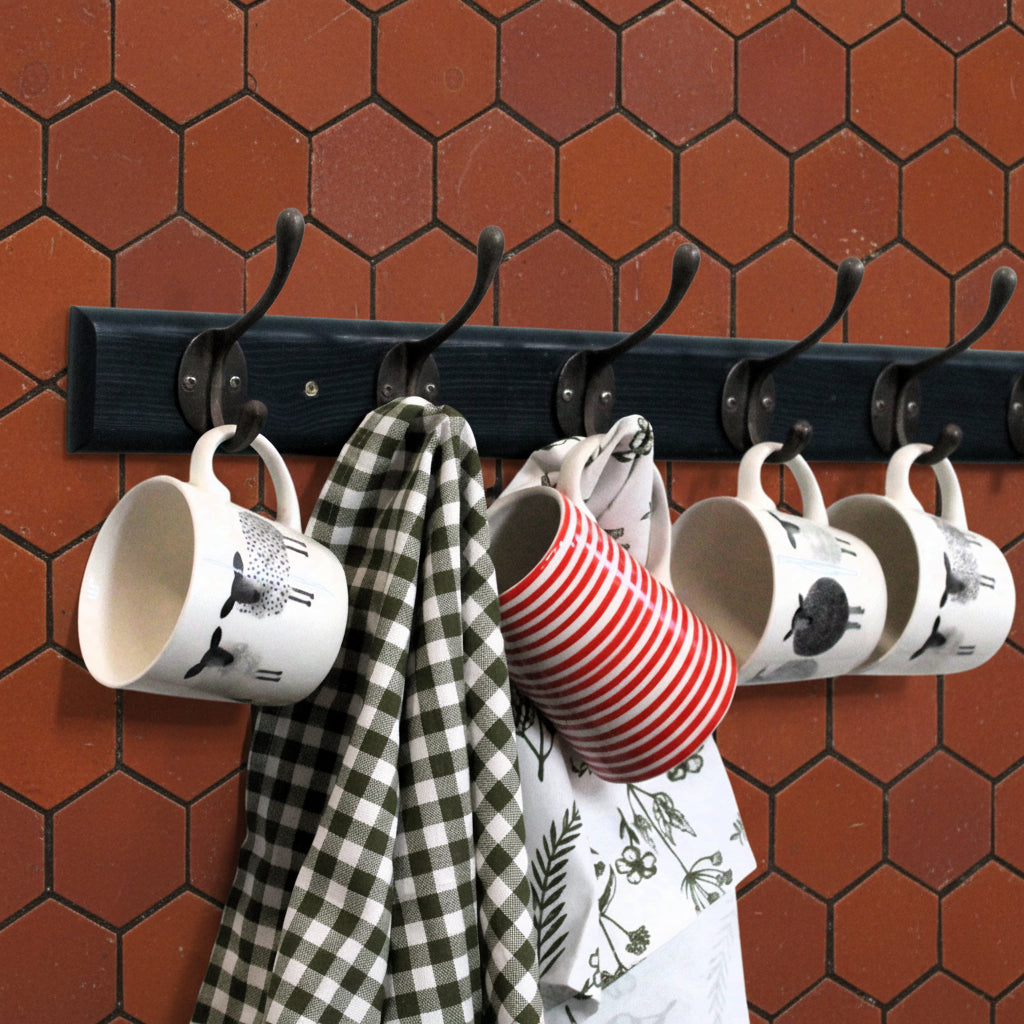 A black wall-mounted hook rack with six curved hooks, shown holding several mugs and towels against a plain white wall.