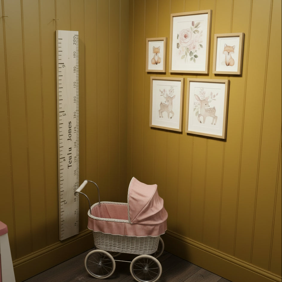 A tall wooden wall ruler with black printed measurements and the text 'Tulips Jones' down the center, leaning against a white wall in a cluttered workshop or storage room.