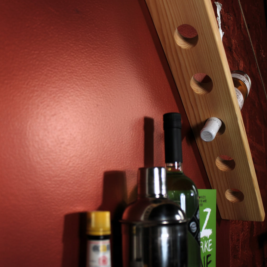 A light natural wood wall-mounted bottle rack with circular cutouts, shown holding several bottles against a red wall.