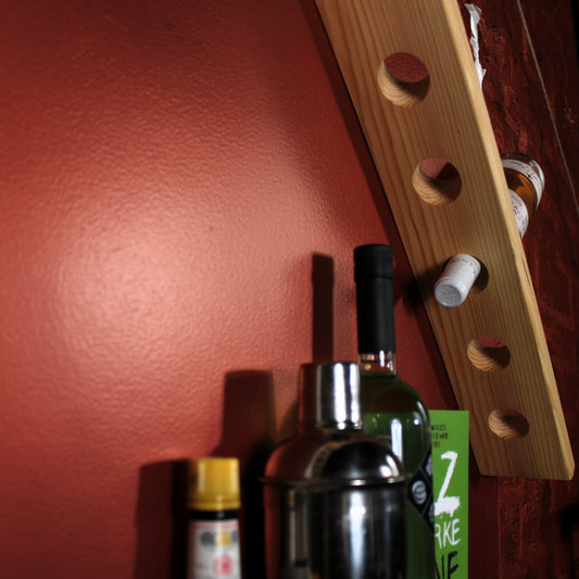 A light natural wood wall-mounted bottle rack with circular cutouts, shown holding several bottles against a red wall.
