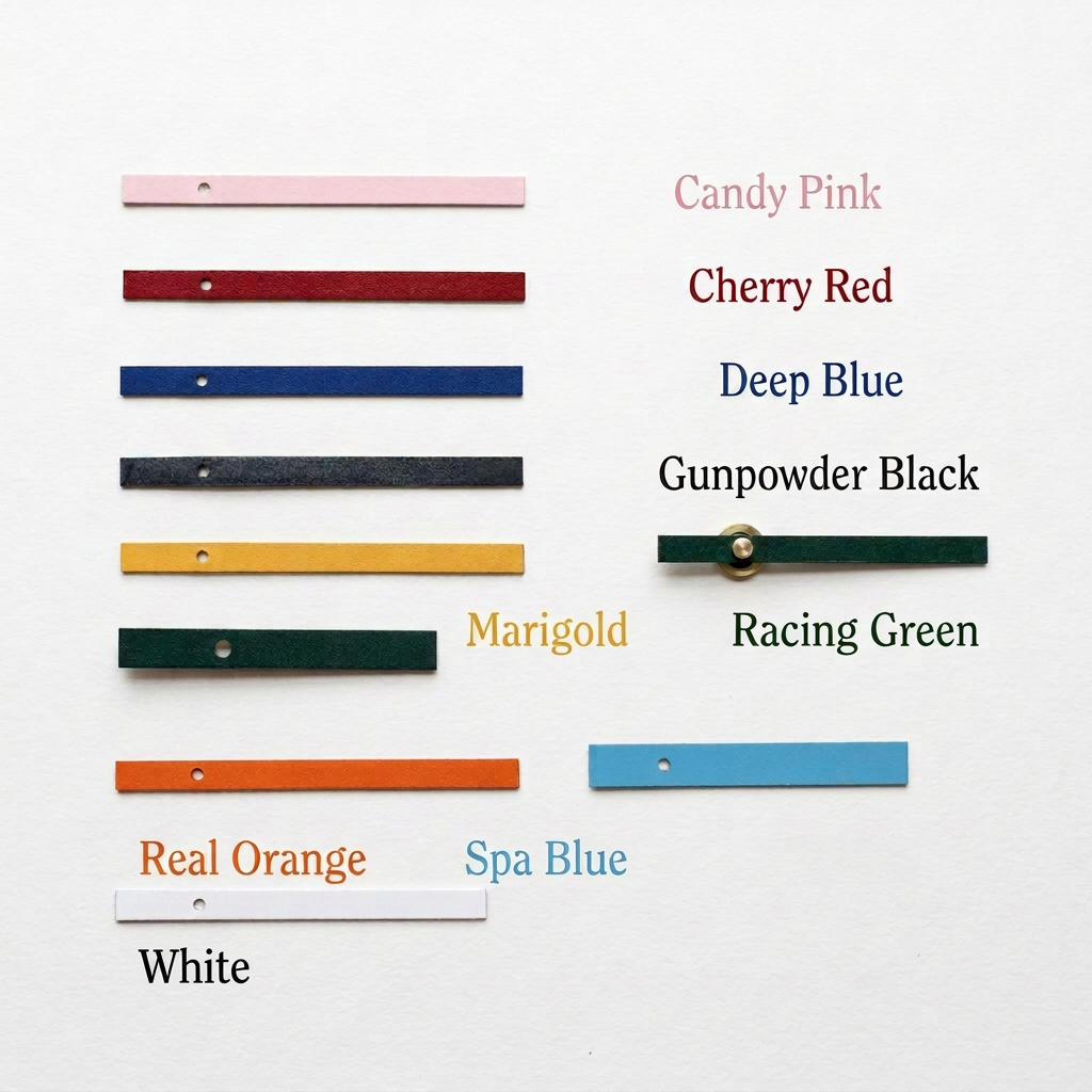 A set of colorful wooden clock hands arranged on a round wooden board with handwritten color labels including Candy Pink, Cherry Red, Deep Blue, Gunpowder Black, Yellow, Racing Green, Spool Blue, and White.
