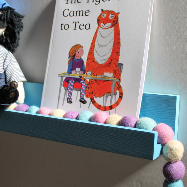 Wooden book ledge painted bright blue and holding a felt garland and children books