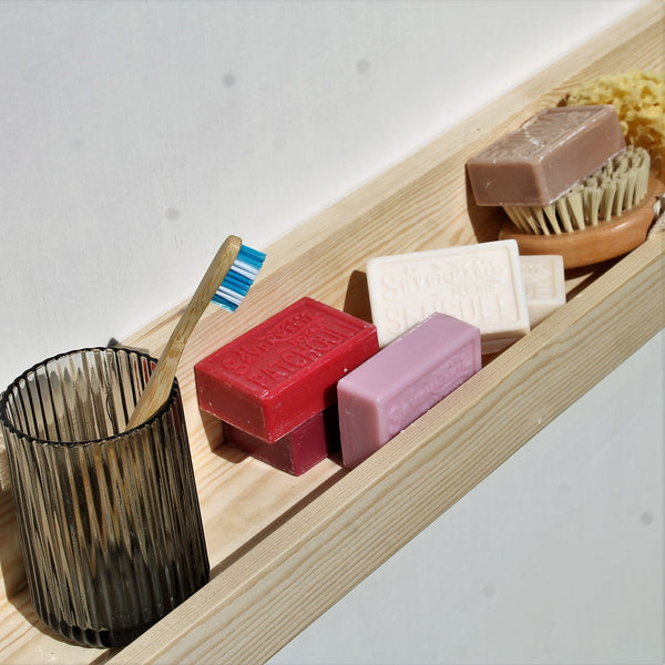 solid wood floating shelf used as bathroom shelf holding soaps, body brush and toothbrush